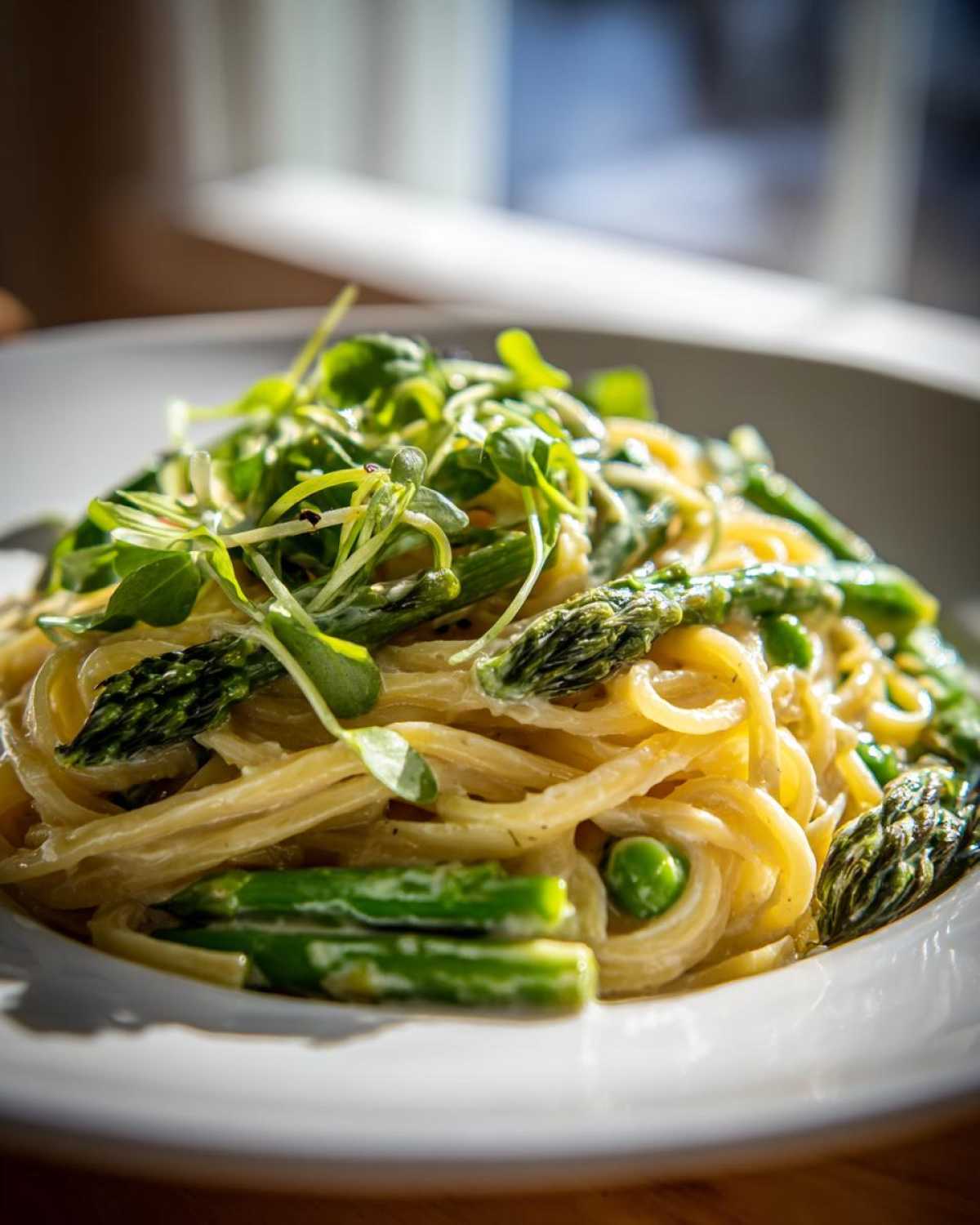 A close-up of creamy Vegan Lemon Asparagus Pasta topped generously with fresh pea shoots.