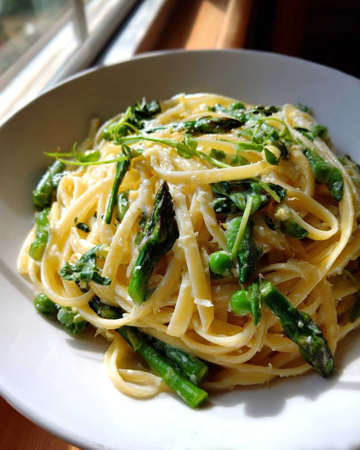 A close-up of creamy Vegan Lemon Asparagus Pasta topped with bright green pea shoots and asparagus tips.