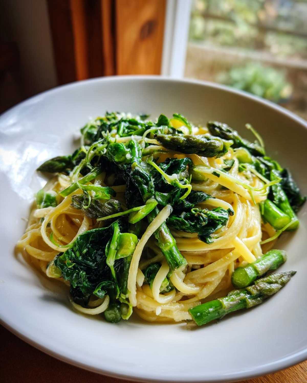Close-up of a bowl of Vegan Lemon Asparagus Pasta with bright green pea shoots and tender asparagus tips.