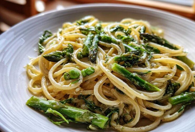 A close-up of creamy Vegan Lemon Asparagus Pasta tossed with bright green asparagus spears and peas.