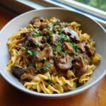 A close-up of Vegan Mushroom Stroganoff served over wide egg noodles and garnished with fresh parsley.