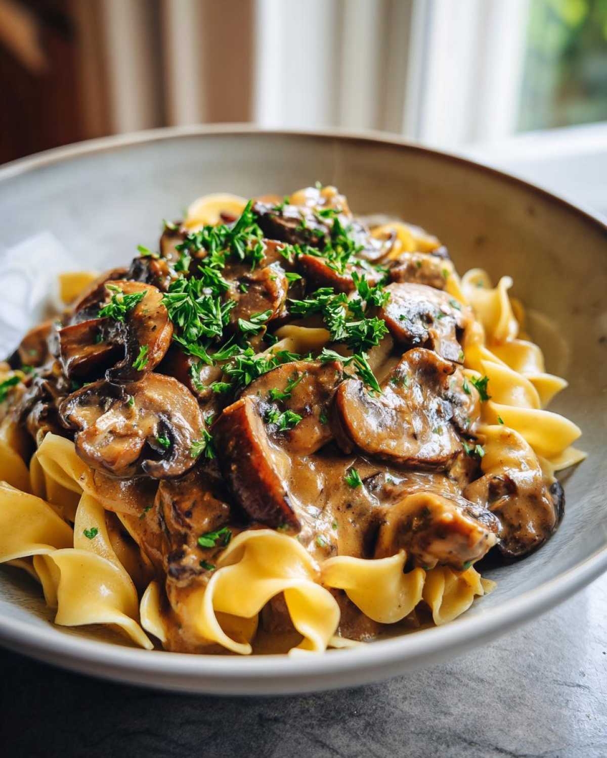 A close-up of Vegan Mushroom Stroganoff served over wide egg noodles and garnished with fresh parsley.