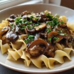 Close-up of Vegan Mushroom Stroganoff served over wide egg noodles and garnished with fresh parsley.