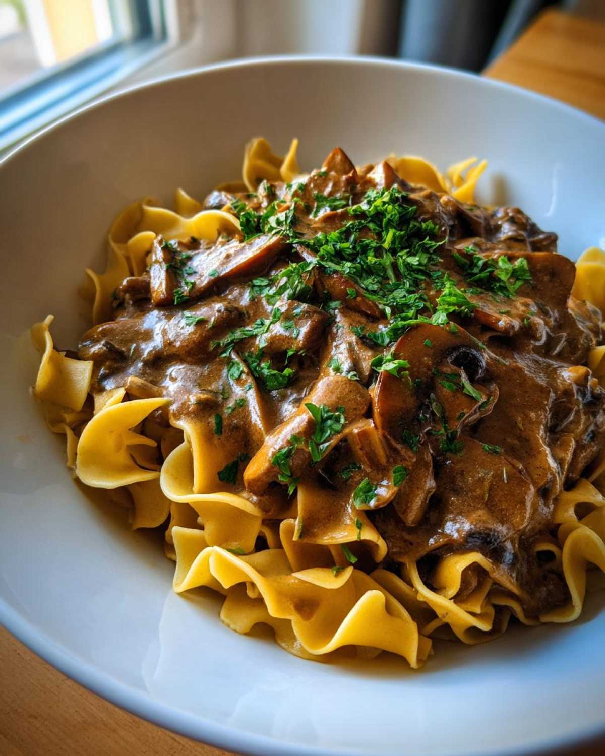 A close-up of Vegan Mushroom Stroganoff served over wide egg noodles and topped with fresh parsley.